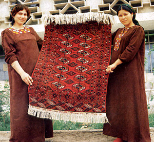 Девушки в туркменской народной одежде показывают туркменский ковер.